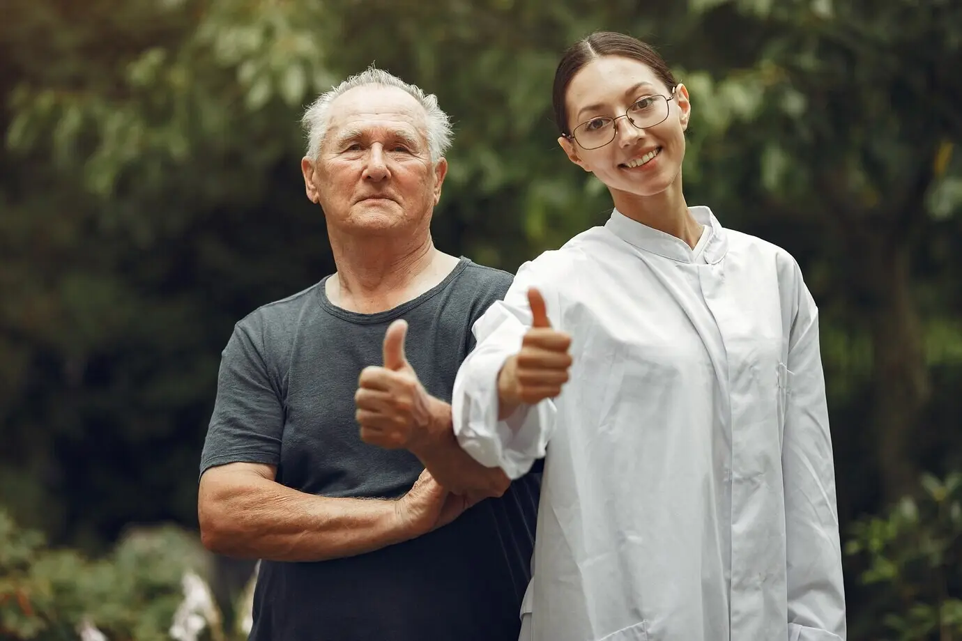 A grandfather in a wheelchair being assisted by a nurse outdoors. An elderly man and a young caregiver in the park.